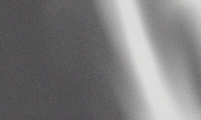 Abstract gray texture featuring a soft diagonal beam of bright white light across a grainy and dark minimalist surface area © Basit