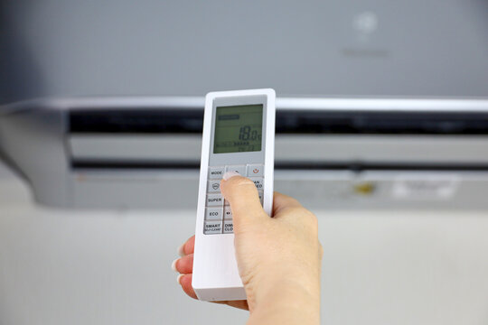 Female hand with remote controller on air conditioner background. Concept of hot weather and home temperature control