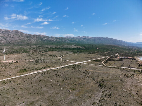 Aerial view of the Suncana elektrana Obrovac solar power plant and wind turbines in a rocky landscape with winding roads in Zaton Obrovacki, Zadar County, Croatia.
