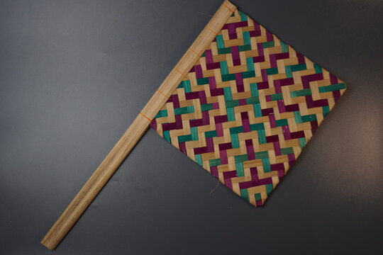 Traditional Indonesian woven bamboo hand fan isolated on a grey background. Colorful satay fan or kipas sate made from braided bamboo skin with geometric pattern, authentic cultural handicraft.