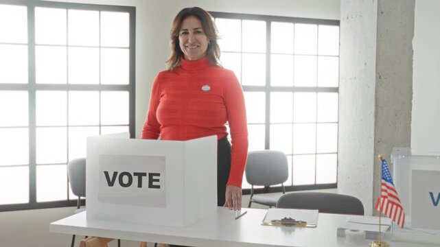 Woman gives thumbs up at a voting booth with visible vote sign and sticker, hand resting on ballot screen in a public building; civic pride.