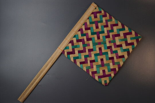 Traditional Indonesian woven bamboo hand fan isolated on a grey background. Colorful satay fan or kipas sate made from braided bamboo skin with geometric pattern, authentic cultural handicraft.