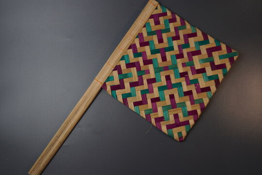 Traditional Indonesian woven bamboo hand fan isolated on a grey background. Colorful satay fan or kipas sate made from braided bamboo skin with geometric pattern, authentic cultural handicraft.