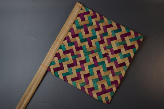 Traditional Indonesian woven bamboo hand fan isolated on a grey background. Colorful satay fan or kipas sate made from braided bamboo skin with geometric pattern, authentic cultural handicraft.