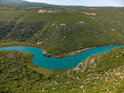 Aerial view of the winding Zrmanja river flowing through a lush green canyon under a clear sky in Zaton Obrovacki, Zadar County, Croatia.