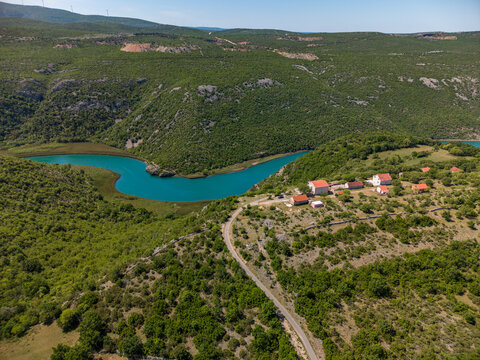Aerial view of the Zrmanja river canyon with turquoise water winding through lush green hills and rural houses in Zaton Obrovacki, Zadar County, Croatia.