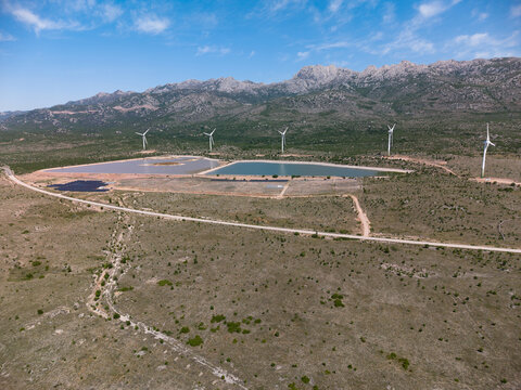 Aerial view of Suncana elektrana Obrovac solar power plant and wind turbines in a rocky landscape under a blue sky in Zaton Obrovacki, Zadar County, Croatia.