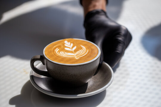 Professional barista hand serving fresh hot latte art coffee on white table