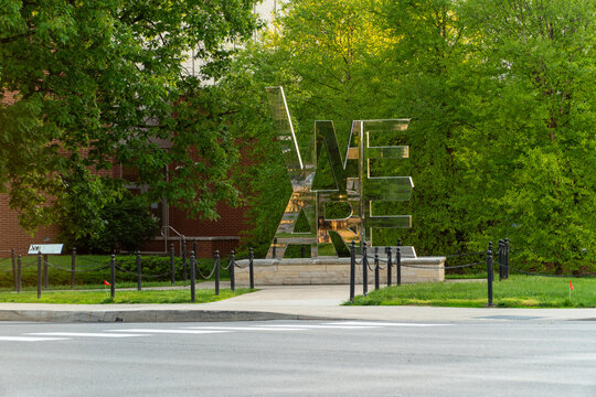 Iconic 'WE ARE' sculpture gleaming amidst vibrant green spring foliage on the historic Penn State University Park campus, symbolizing school pride and tradition.