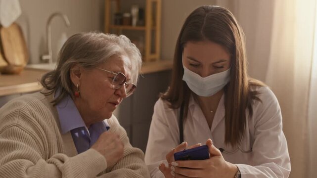 Slow motion of brunette healthcare worker helping elderly woman with smartphone, showing application for monitoring blood sugar
