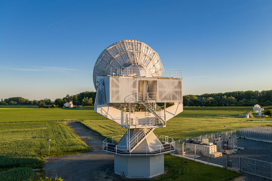 Aerial view of Satelliten-Messstelle Leeheim with its large parabolic antenna surrounded by green fields and trees under a clear blue sky in Riedstadt, Hessen, Germany.