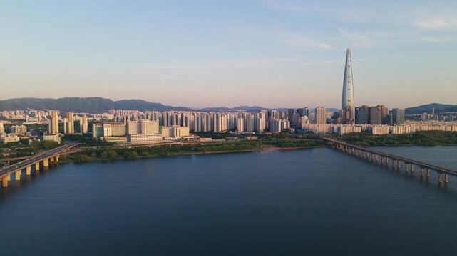 Aerial approach to Jamsil Railway Bridge over wide Han River with Lotte Tower and Seoul skyline at golden sunset in South Korea