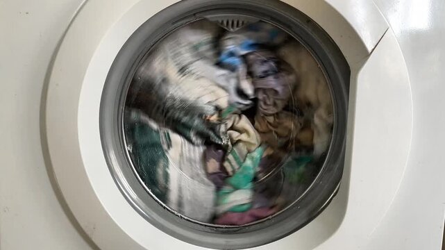 Close up of washing machine drum with rotating laundry and detergent capsule. Modern washing machine cleaning apparel at home. Front load washer process with wet clothes for domestic hygiene.