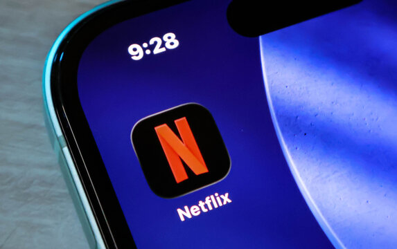 Closeup of the netflix mobile application icon on an iphone screen with a blue wallpaper background