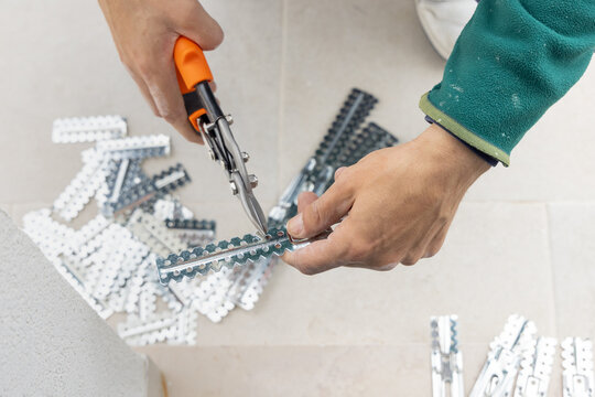 Drywall worker cutting metal profile with tin snips during suspended ceiling installation, hands close up