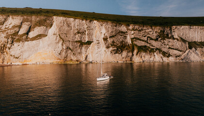 Sailboat anchored in calm water near high white cliffs at sunset © Reuben