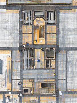 Aerial view of a construction site with workers in hard hats walking on a rebar grid and wooden platforms in Taiwan.