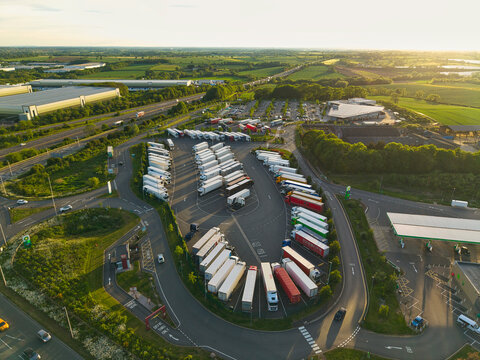 Aerial view of Rugby Services motorway station with rows of parked trucks and a gas station surrounded by green fields at sunset Rugby, England, United Kingdom.
