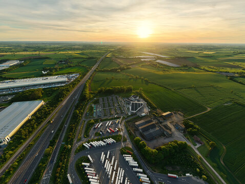 Aerial view of Rugby Services featuring trucks parked in rows and the M6 motorway under a golden sunset in Rugby, England, United Kingdom.