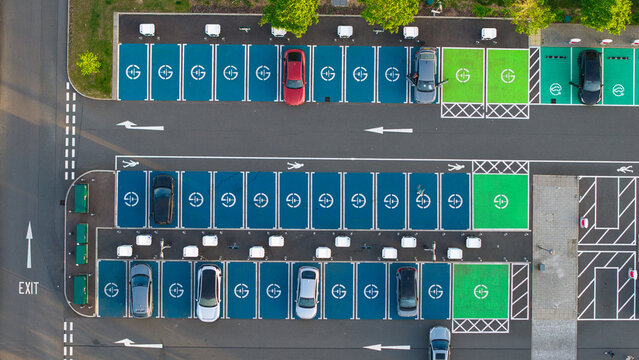 Aerial view of Rugby Services electric vehicle charging station with cars parked in blue and green bays under bright daylight in Rugby, England, United Kingdom.
