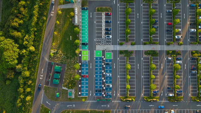 Aerial view of Rugby Services featuring electric vehicle charging stations with green and blue bays, parked cars, and rows of trees Rugby, England, United Kingdom.