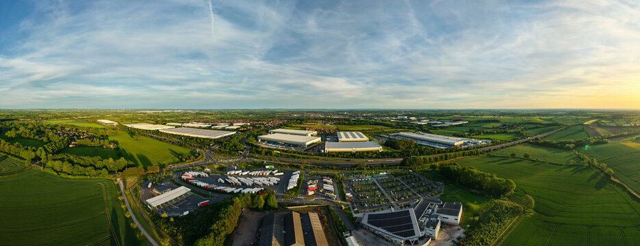 Aerial view of Rugby Services motorway service station with large parking areas, industrial warehouses, and surrounding green fields Rugby, England, United Kingdom.