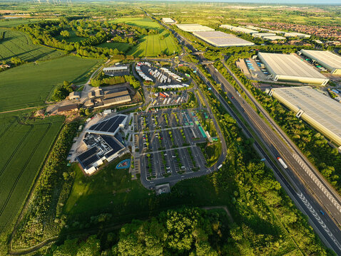 Aerial view of Rugby Services featuring modern facilities, solar panels, and extensive parking areas next to the M6 motorway and green fields Rugby, England, United Kingdom.