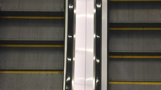 Pair of empty moving metal escalators with yellow safety lines photographed from above