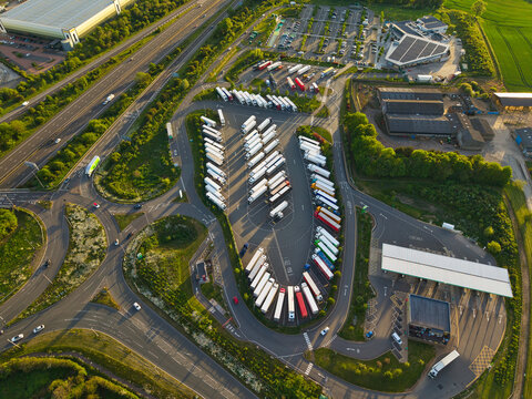Aerial view of Rugby Services motorway station with rows of parked trucks and the M6 motorway surrounded by green fields in Rugby, England, United Kingdom.