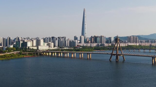 Aerial parallax approach rising above Olympic Bridge cable-stayed pylon with Lotte Tower and wide Seoul cityscape over Han River in South Korea