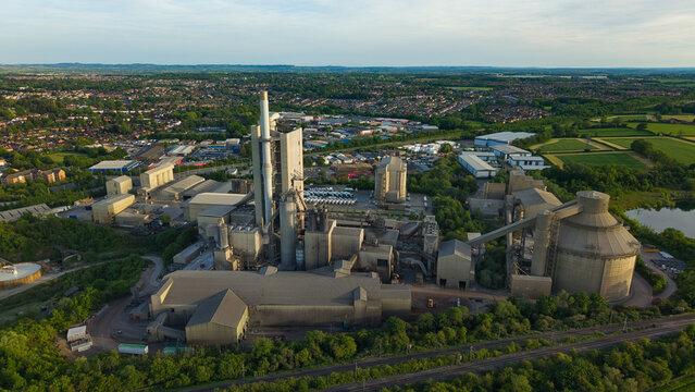 Aerial view of the Rugby Cement Plant featuring tall industrial chimneys and large silos surrounded by lush green landscape in Rugby, England, United Kingdom.