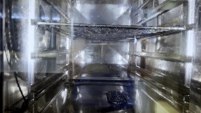 Commercial kitchen combi steamer oven in the cleaning process inside a professional restaurant. Automated self-cleaning mode washing the stainless steel interior racks and glass door with water