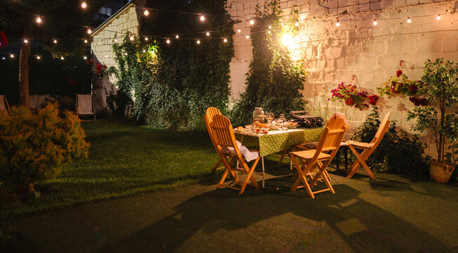 Backyard dinner party setup with string lights at night