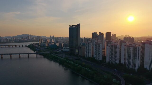 Aerial pull back along Han River at golden sunset revealing silhouetted Seoul riverside apartments and bridges in warm sunlight South Korea
