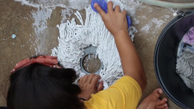 A girl washes the head of a spin mop on concrete