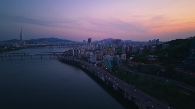 Aerial pullback along Gangbyeonbuk-ro Expressway above Han River revealing busy nighttime traffic in Seoul after sunset at blue hour South Korea