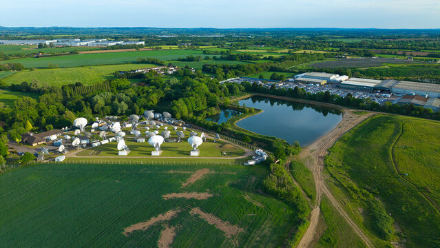 Aerial view of the Satellite Mediaport with numerous parabolic antennas surrounded by lush green fields and a small pond in Long Lawford, England, United Kingdom.