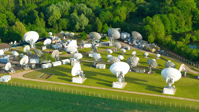 Aerial view of the Satellite Mediaport featuring numerous large parabolic antennas arranged on a green lawn surrounded by dense woodland in Long Lawford, England, United Kingdom.
