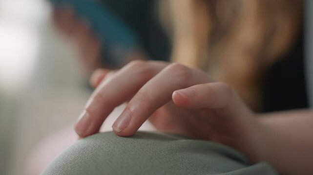 Closeup hand on green cushion with blurred figure, gentle tapping and light pressure, student gesture while scrolling phone, warm indoor light, emphasis on motion and textile texture