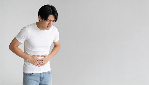 Asian man suffering from abdominal pain and clutching his stomach. Young guy experiencing stomach ache or indigestion. Health crisis, medical symptom, and human suffering concept with copyspace.