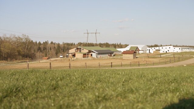Farm buildings and structures stand amidst green fields under a clear sky, representing agricultural production, sustainable living, and modern farming practices in a countryside setting