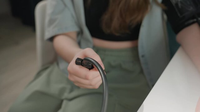 Young caucasian woman preparing blood pressure cuff on arm, sitting at white table with casual green trousers, holding tubing with tentative grip, natural soft light, focused expression during athome