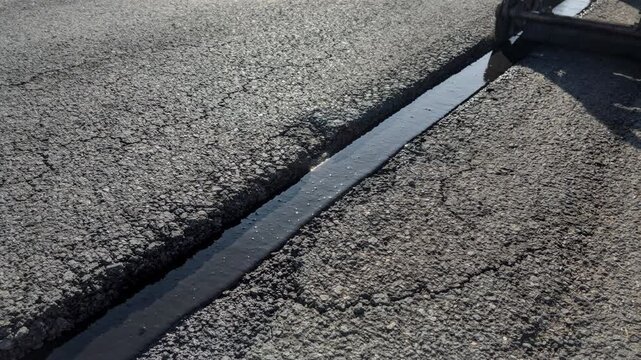 Medium shot capturing edge seal process on asphalt seam highlighting smooth compaction and material bonding under sunlight.