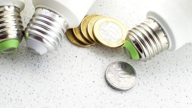 Bright light bulb on Brazilian coins, illustrating the concept of economy and its implications on the electricity bill.