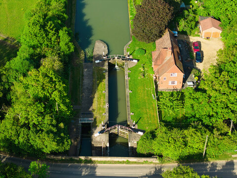 Aerial view of the Grand Union Canal lock gates surrounded by a red brick house and dense green trees in Bridge 31, England, United Kingdom.