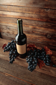 Red wine bottle with blue grapes on an old wooden table.