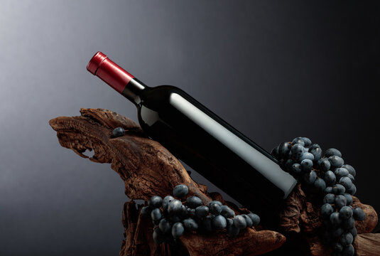 Unopened bottle of red wine, blue grapes, and weathered snag.