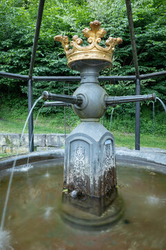 Historic iron fountain with a golden crown and streaming water in a green park. Koenigsbronn, Baden-Wuerttemberg, Germany.
