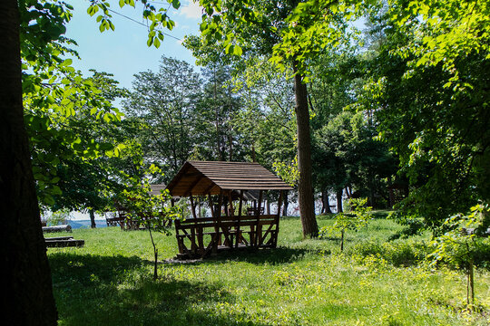 Wooden gazebo in a lush summer park surrounded by green trees and sunlight offering a peaceful place for outdoor relaxation and recreation.