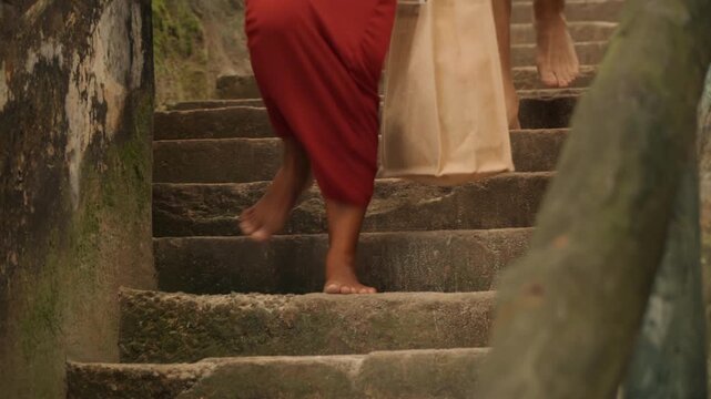 Walking barefoot through lush nature. Pair meanders down oceanfront tropical trail barefoot. Two individuals casually walking without shoes on scenic tropical seaside trail with shopping bags
